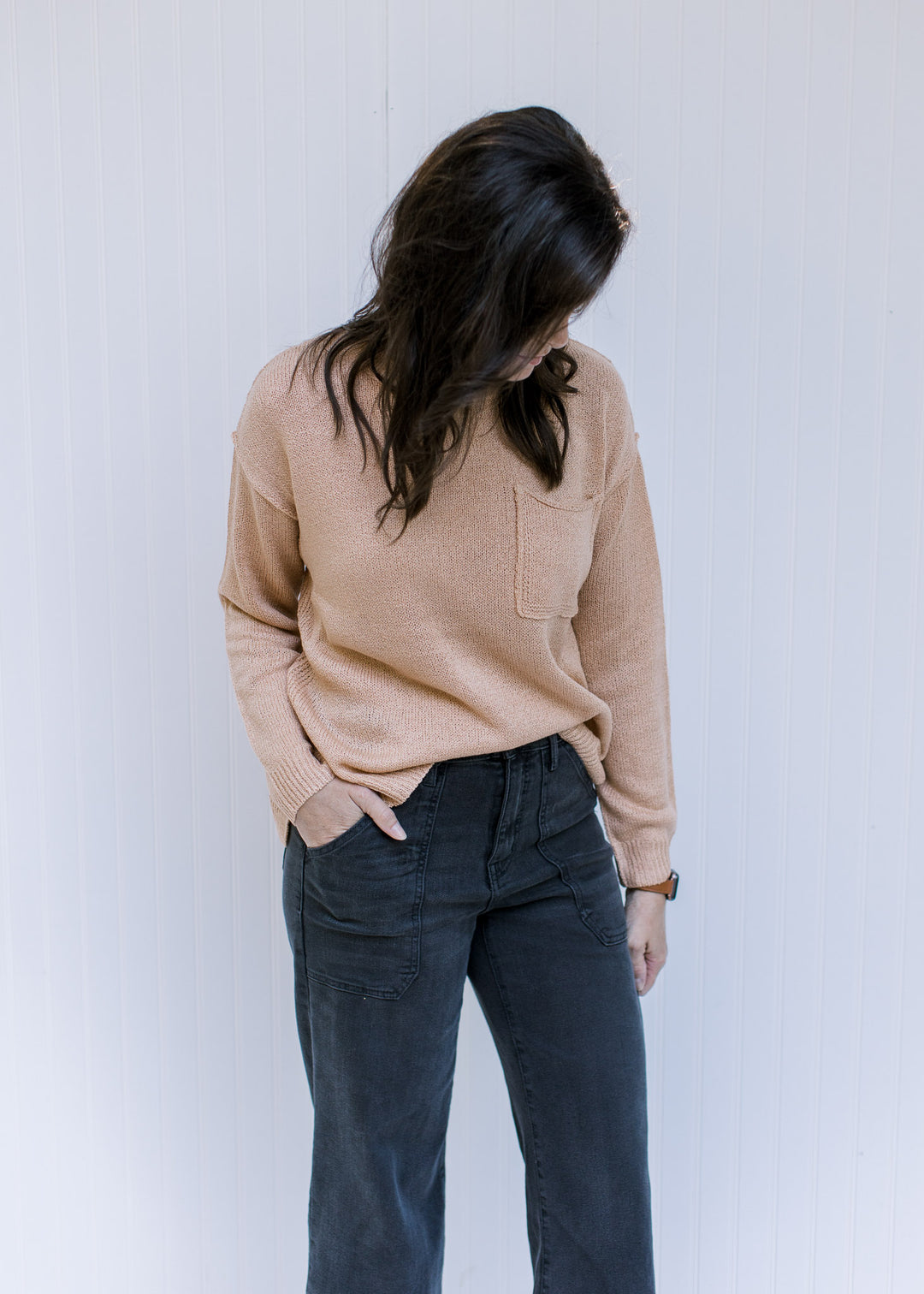 Model wearing an acrylic amber colored sweater with a patch pocket, exposed hem and long sleeves. 
