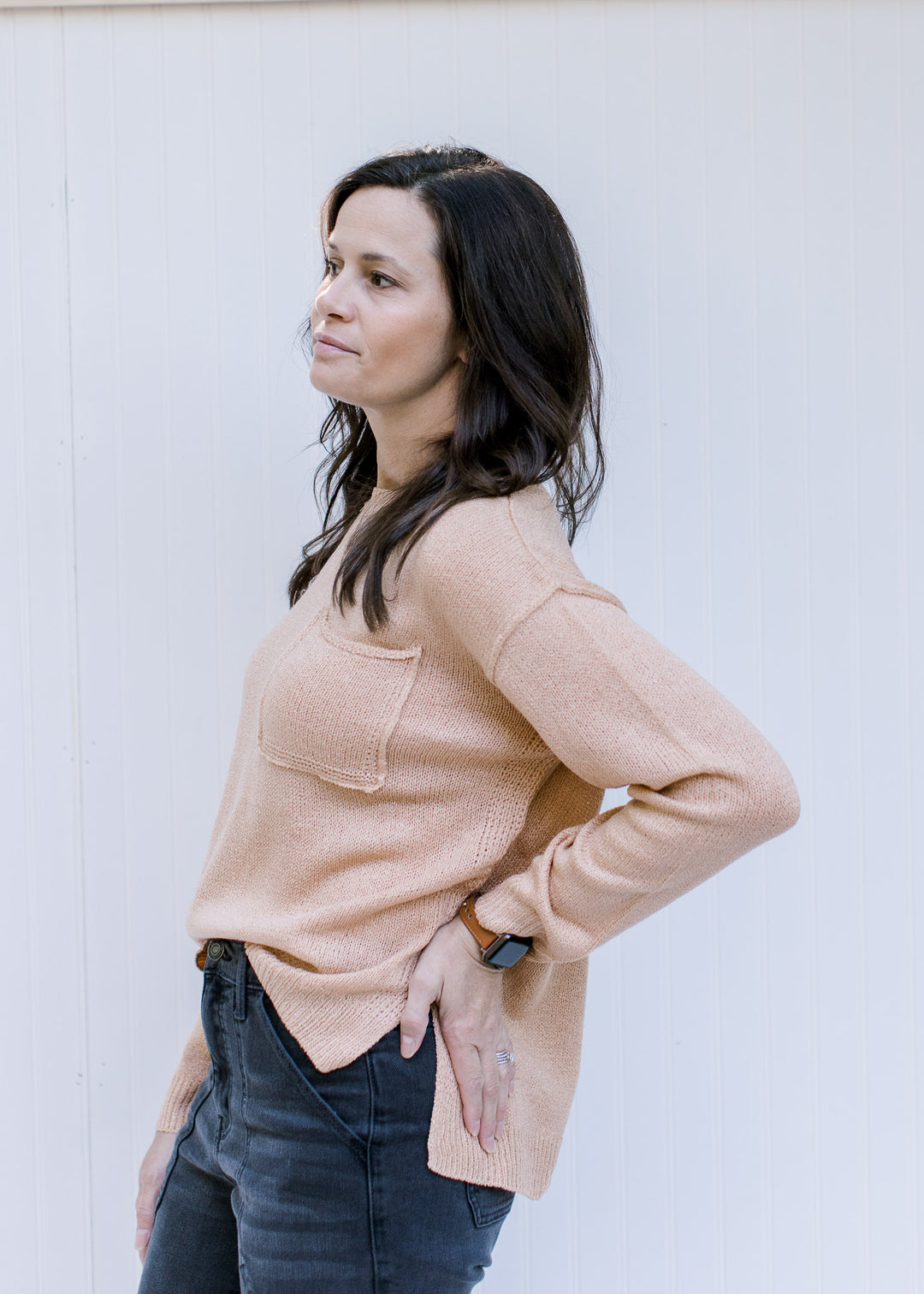 Side view of Model wearing an amber sweater with a patch pocket, exposed hem and long sleeves.