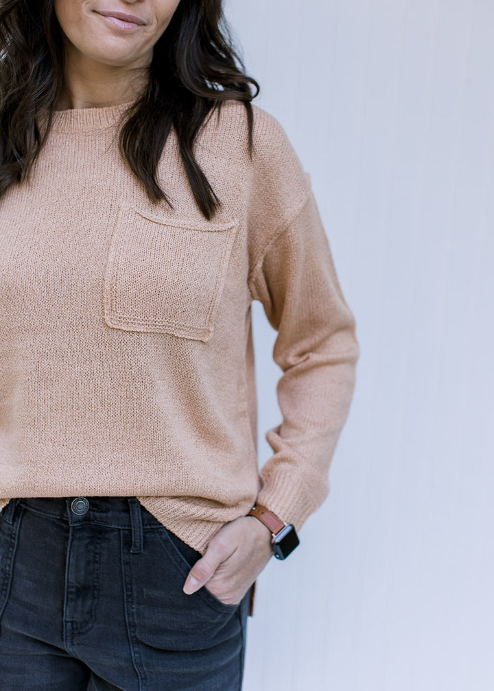 Close up of patch pocket on an amber sweater with exposed hem, long sleeves and a round neck.