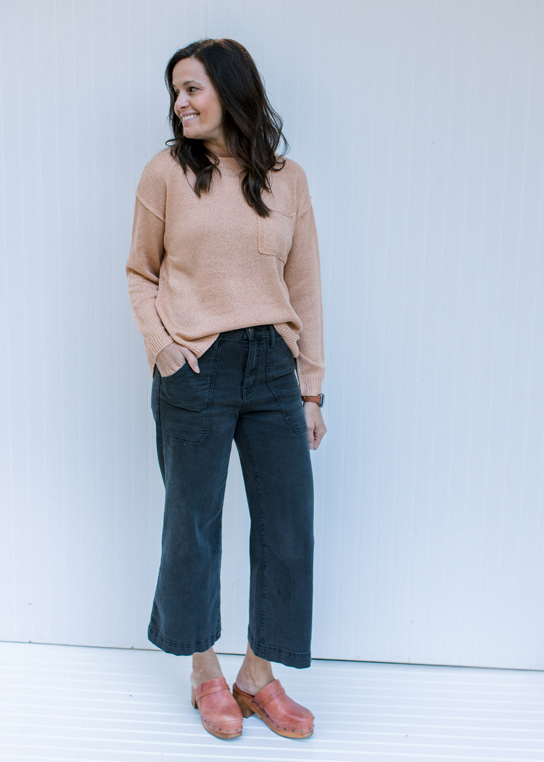 Model wearing jeans and mules with an amber colored sweater with exposed hem and long sleeves. 