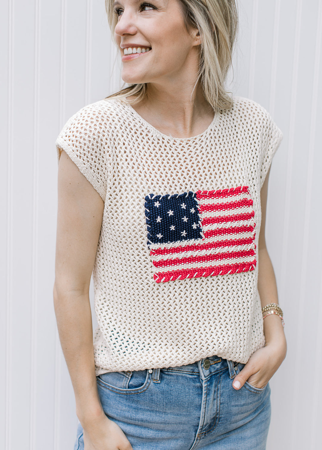Model wearing a cream crochet sweater with American flag, capped short sleeve and a round neck.