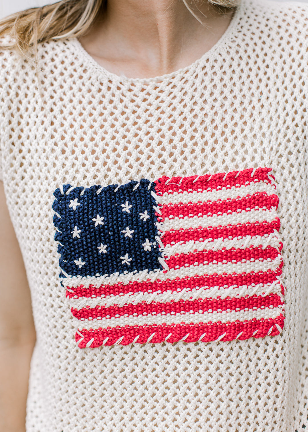 Close up of American flag on the front of a crochet cream sweater with capped sleeves. 