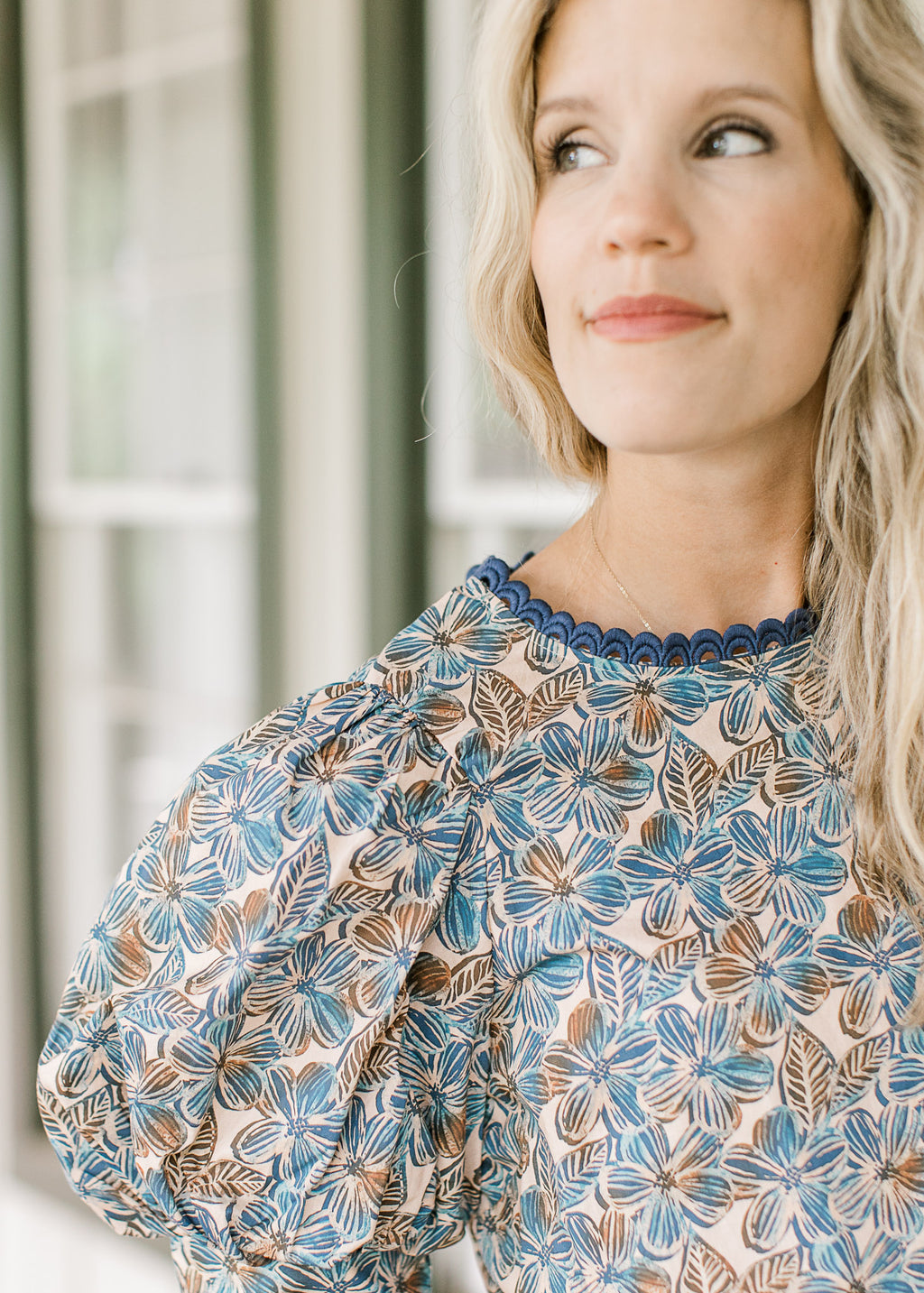 Close up of navy lace at the neck of a short sleeve cream top with blue and brown floral. 