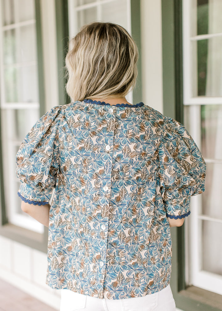 Back view of Model wearing a tan top with blue and brown floral and button back.