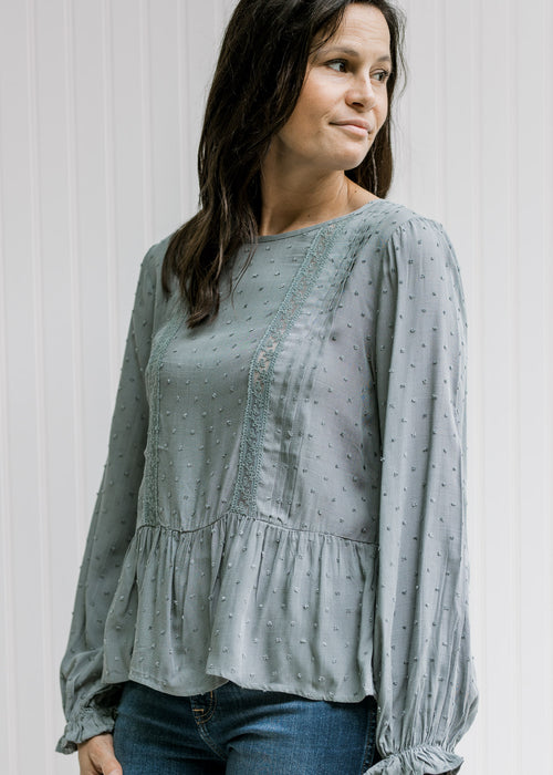 Model wearing a dotted dusty blue top with a lace detail and long sleeves with elastic wrist. 