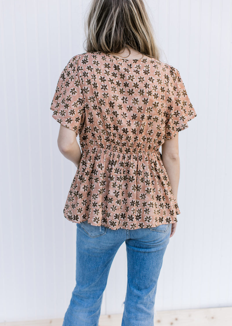 Back view of Model wearing an apricot peplum top with a brown floral pattern and short sleeves.