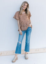 Model wearing jeans, mules and an apricot peplum top with a brown floral pattern and short sleeves.