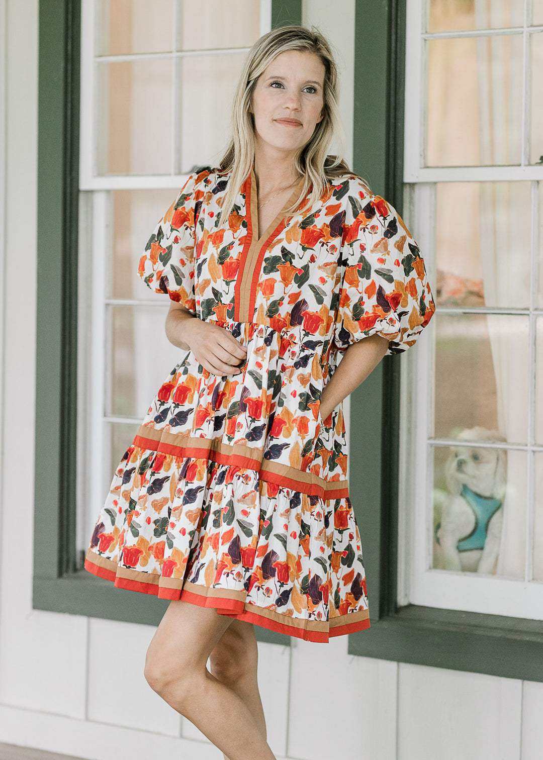 Model wearing an above the knee cream dress with rust, brown and green floral and bubble sleeves. 