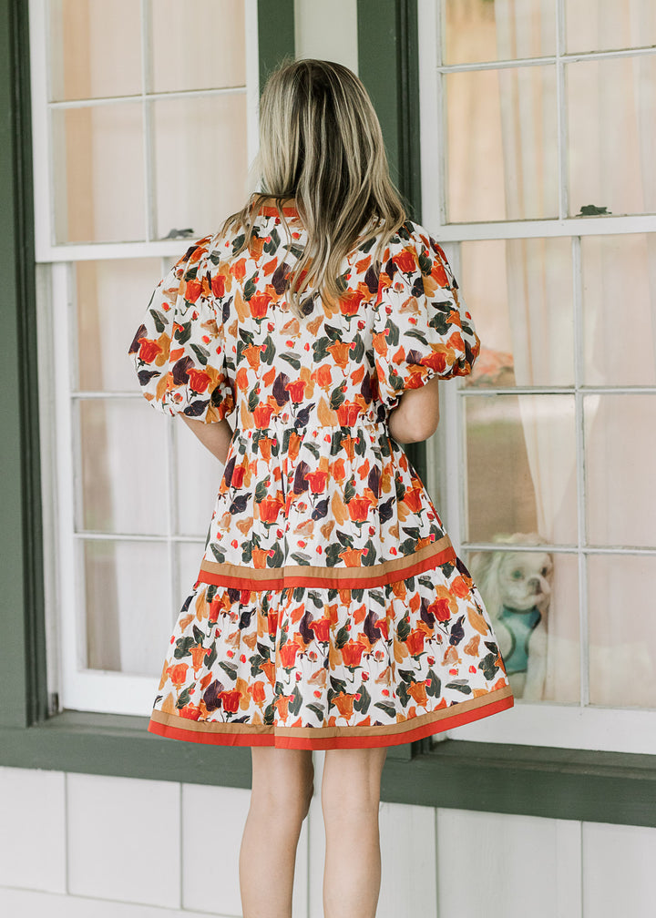 Back view of model wearing a cream dress with fall floral hues and bubble short sleeves. 