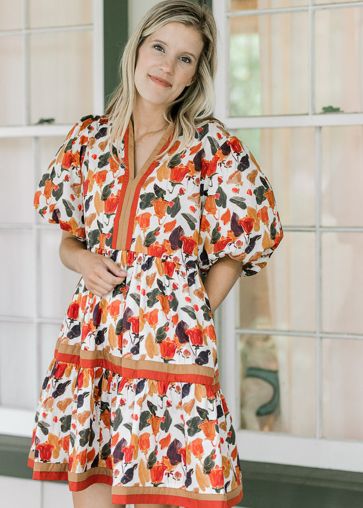 Model wearing a cream v-neck dress with fall hues, bubble short sleeves and pockets. 