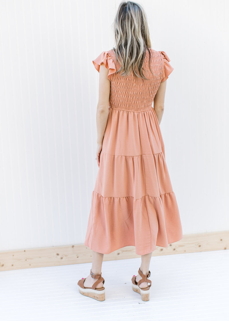 Back view of Model wearing an apricot midi with a smocked bodice, capped sleeves and a v-neck.