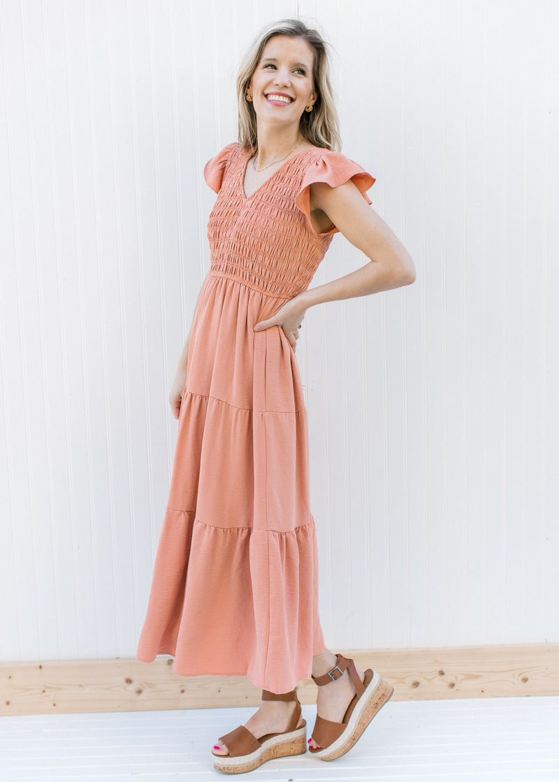 Model wearing a tiered apricot midi with a smocked bodice, ruffle capped sleeves and a v-neck.