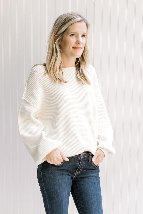Model wearing an ivory yarn sweater with long sleeves, exposed shoulder seam and a boat neck. 