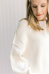 Close up of exposed hem and boat neck on a model in a long sleeves ivory yarn sweater. 