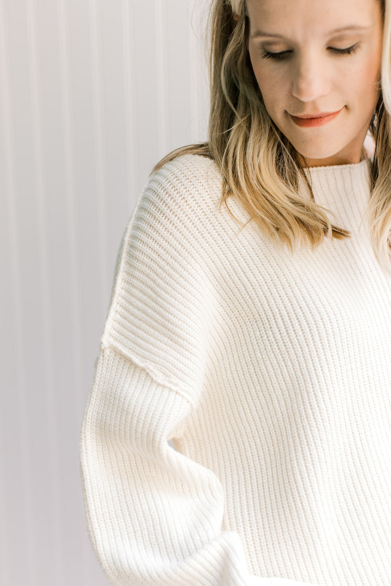 Close up of exposed hem and boat neck on a model in a long sleeves ivory yarn sweater. 