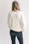 Back view of Model wearing an ivory yarn sweater with long sleeves and exposed shoulder seam. 