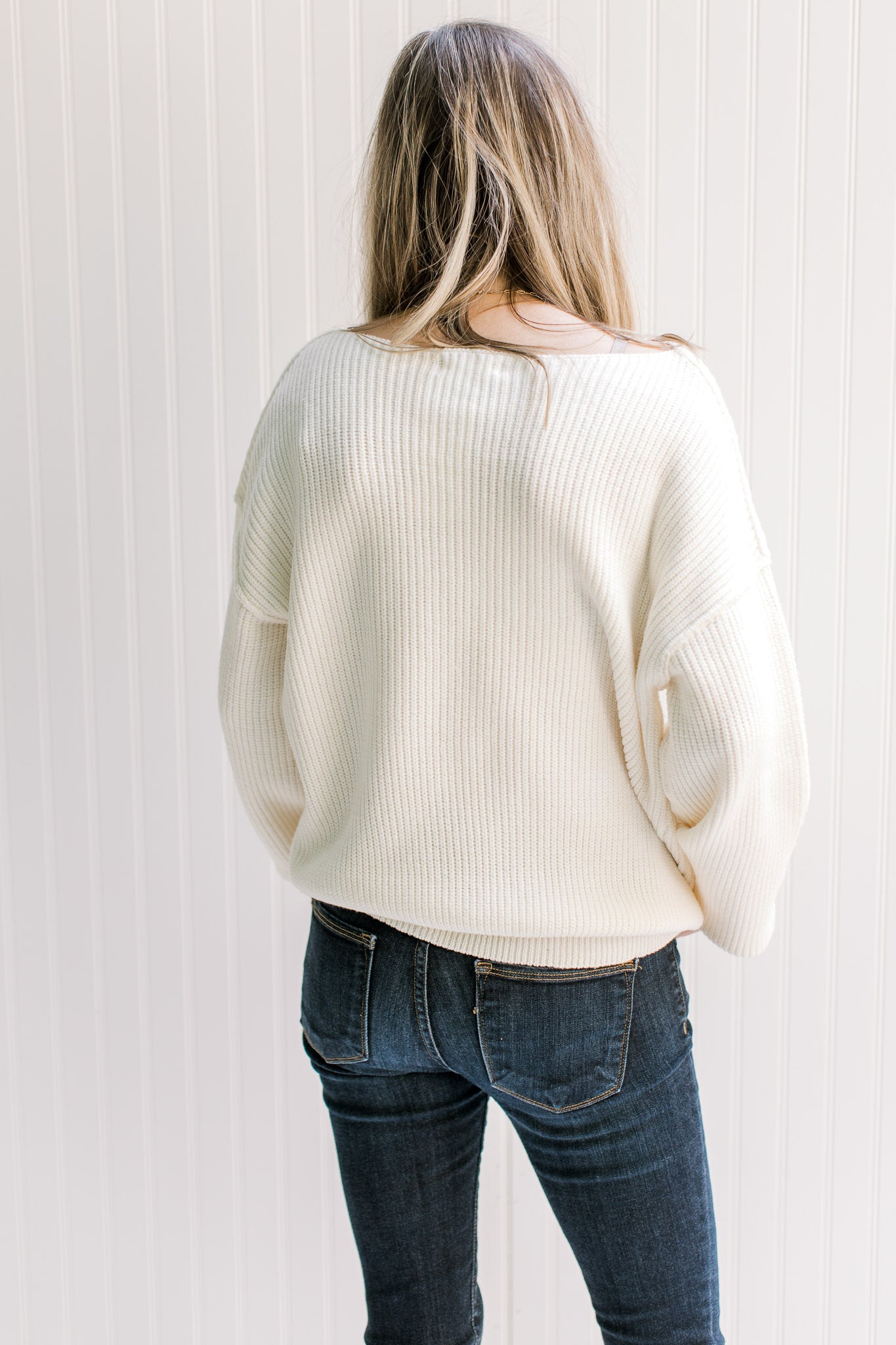 Back view of Model wearing an ivory yarn sweater with long sleeves and exposed shoulder seam. 