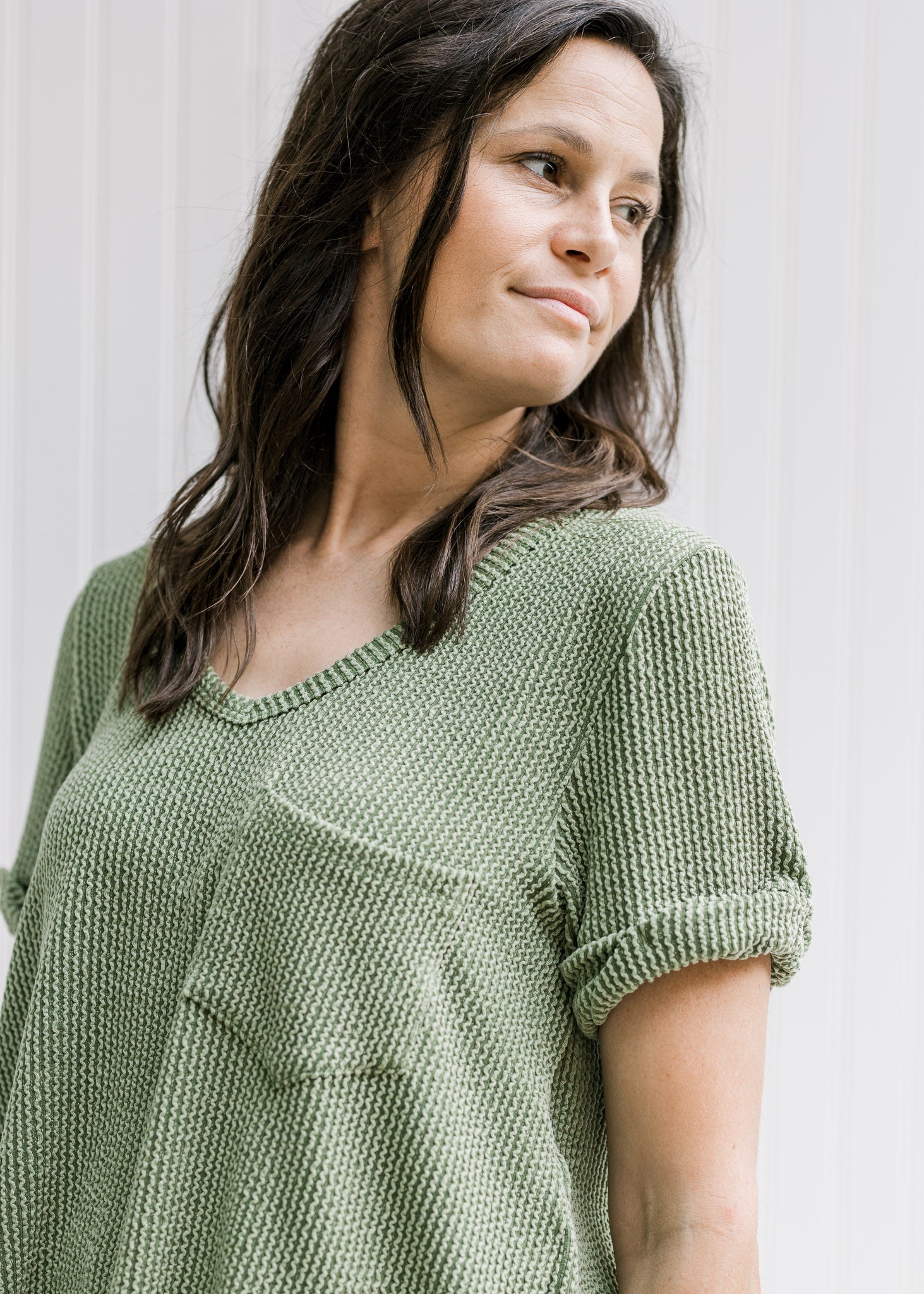 Model wearing a green corded v-neck top with a patched pocket and cuffed short sleeves. 