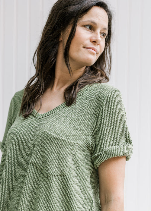 Model wearing a green corded v-neck top with a patched pocket and cuffed short sleeves. 