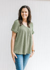 Model wearing jeans with a green corded v-neck top with a patched pocket and cuffed short sleeves. 