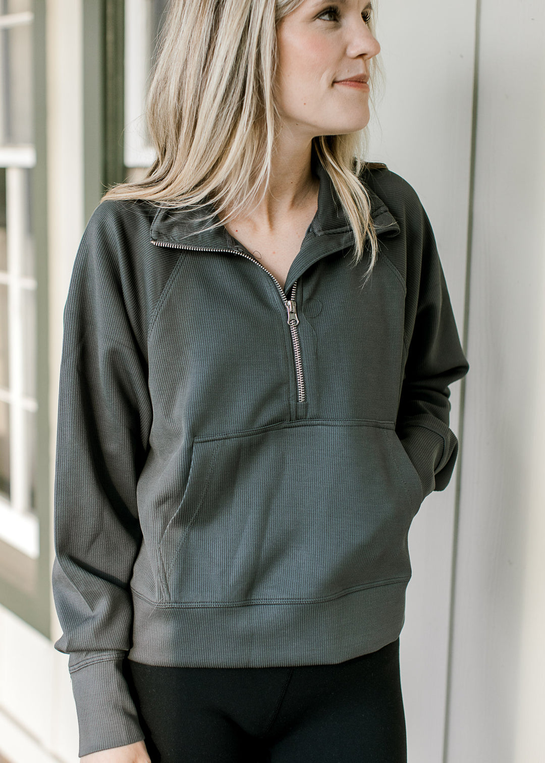 Model wearing an ash gray ribbed pullover with a quarter zip, front pouch pocket and long sleeves. 