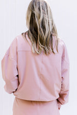 Back view of Model wearing a fleece lined, dusty pink pullover with zipper pockets and long sleeves.