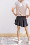 Back view of Model wearing a black pleated skort with elastic waistband and built in shorts.