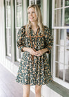 Model wearing a black floral dress with a v-neck and a tie, short sleeves and ruffle detail at neck.