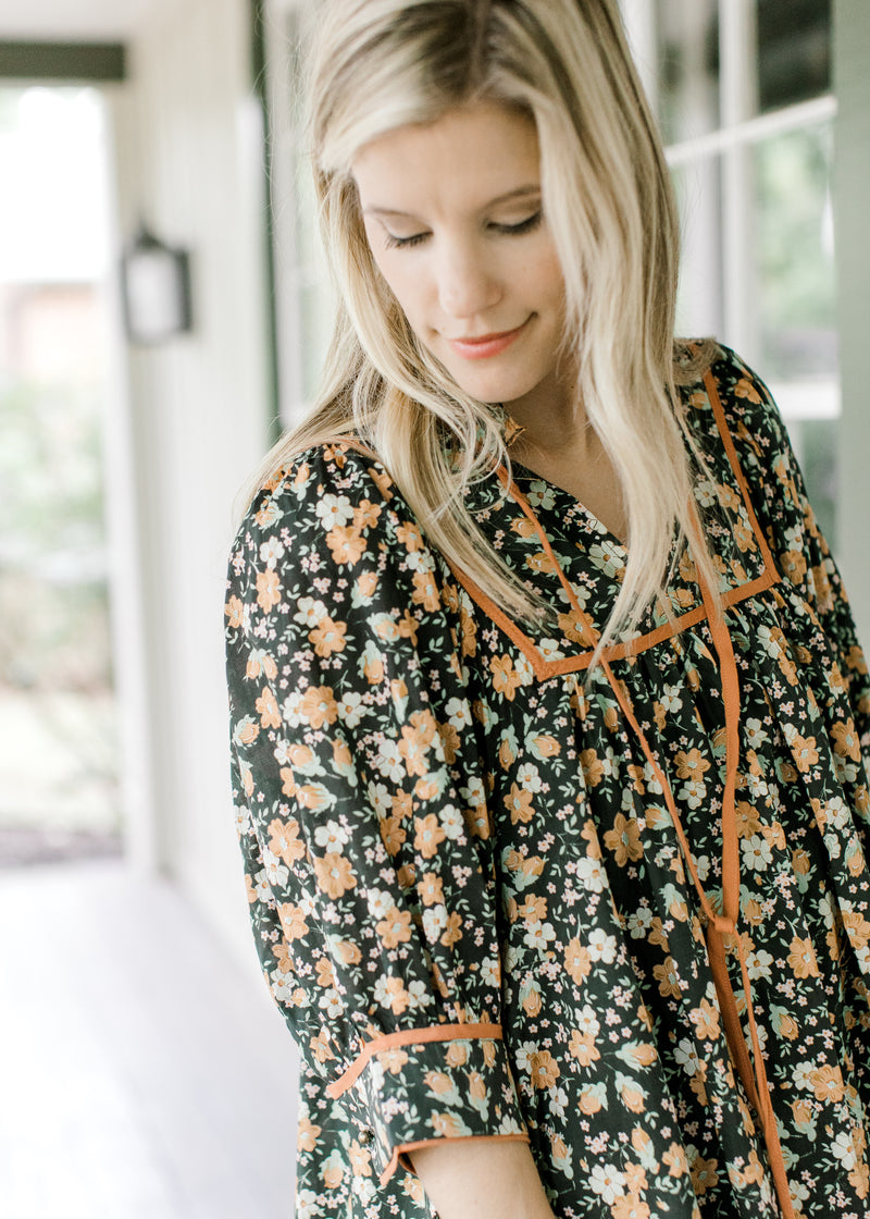 Close up of v-neck with tie and ruffle detail at neck of a black floral dress with short sleeves. 