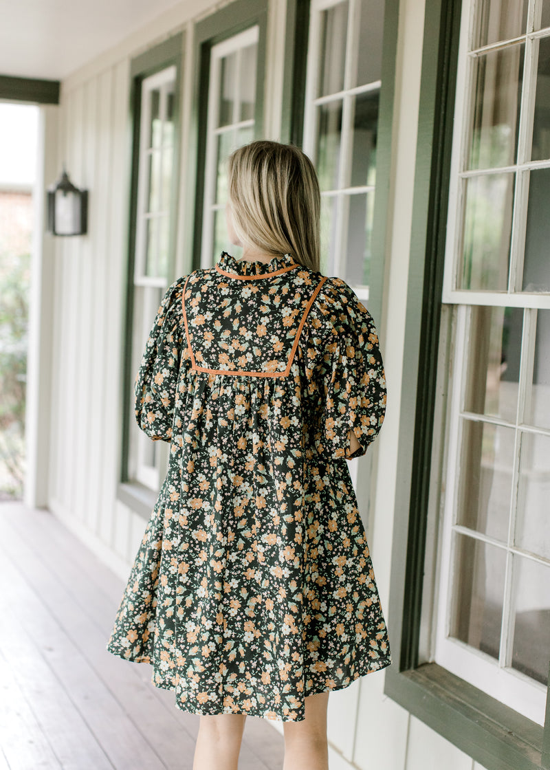 Back view of Model wearing a black floral dress with a v-neck, short sleeves and babydoll fit.