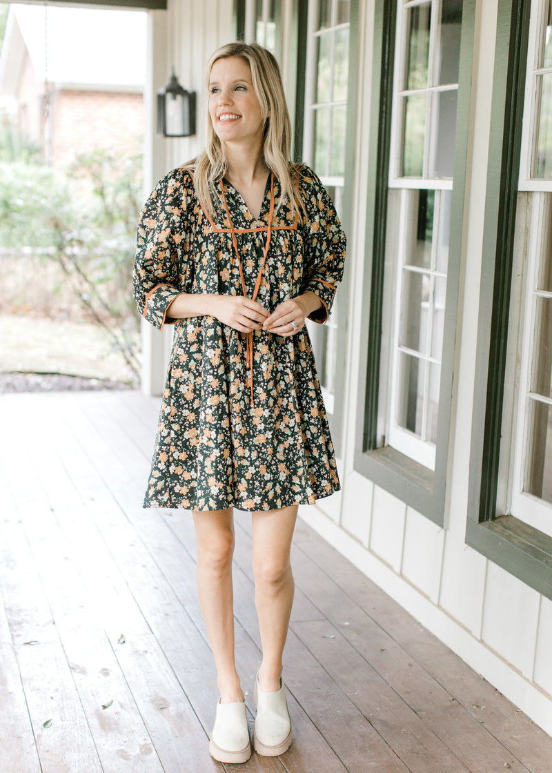 Model wearing mules and a black floral dress with a v-neck and a tie and short sleeves.