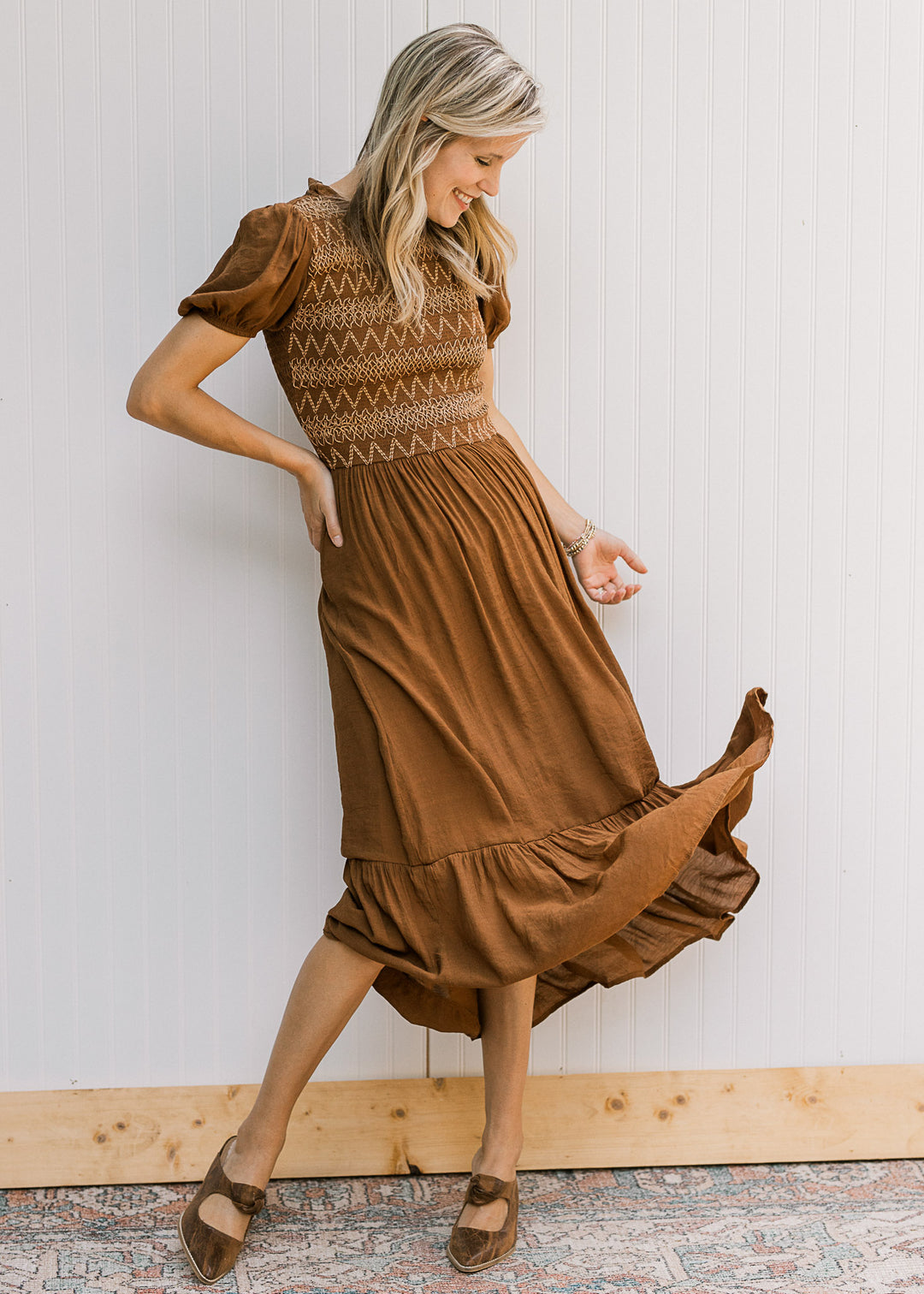 Model wearing a brown midi with taupe embroidery on a smocked bodice and short sleeves. 