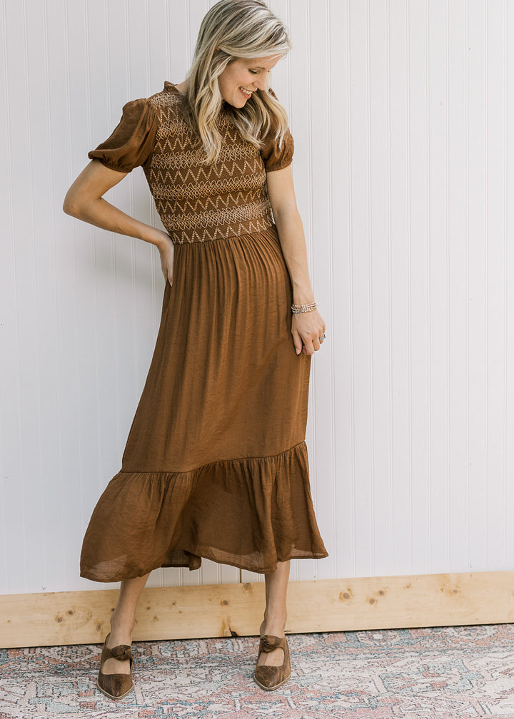 Model wearing heels and a brown midi with embroidered smocked bodice and short sleeves. 