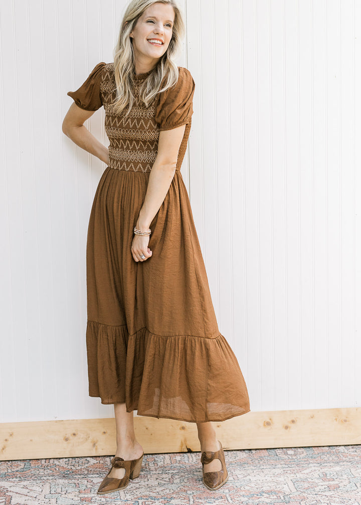 Model wearing a brown lined midi with taupe embroidery on a smocked bodice and short sleeves. 