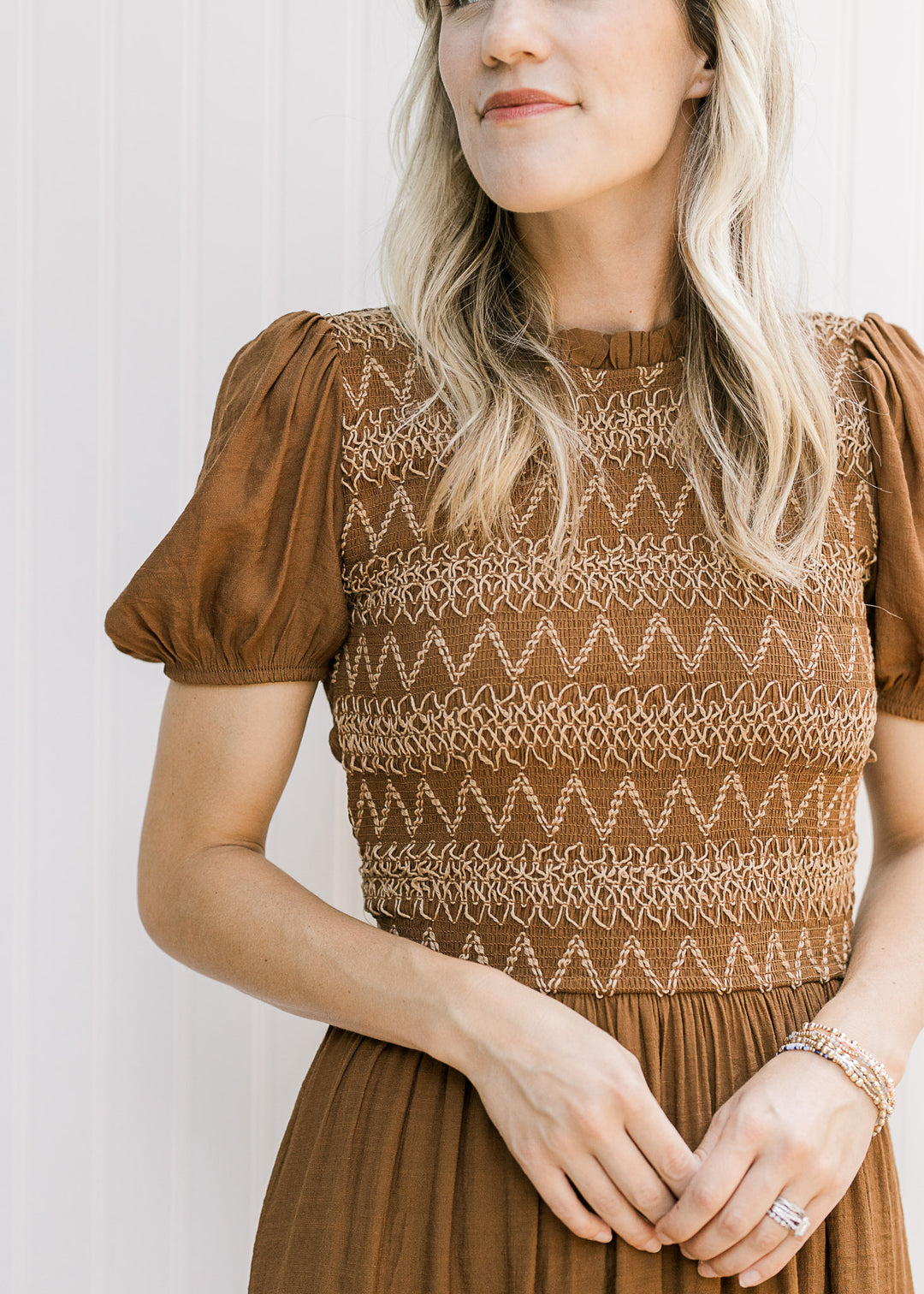 Close up of taupe embroidery on the smocked bodice of a brown midi with short sleeves. 