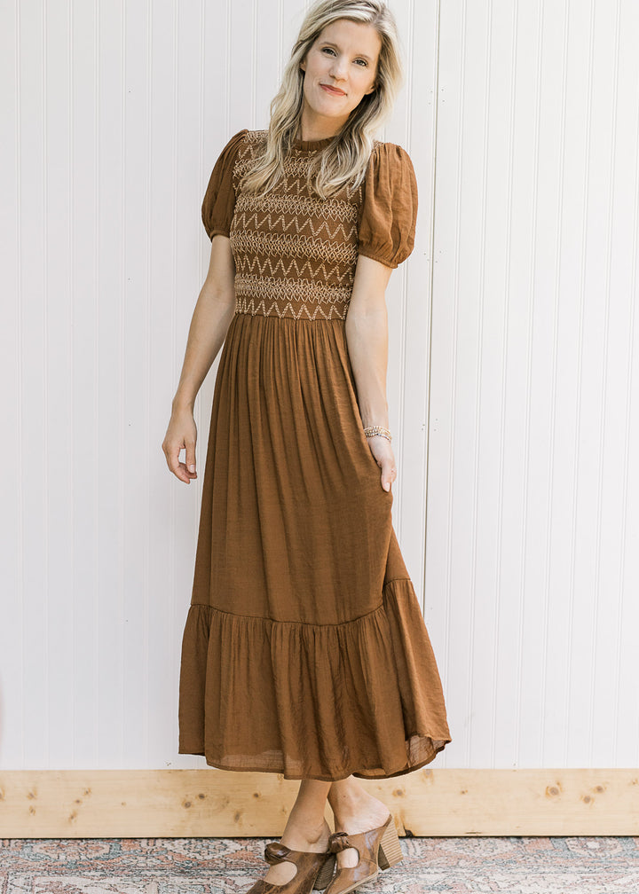 Model wearing a flowy brown midi with taupe embroidery on a smocked bodice and short sleeves. 