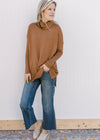 Model wearing jeans, mules and a camel sweater with long sleeves, cowl neck and split sides. 