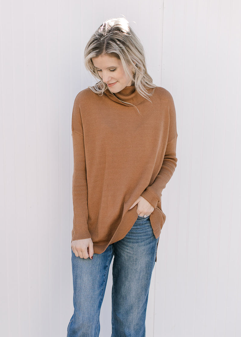 Model wearing jeans with a camel flowy sweater with long sleeves, cowl neck and split sides. 