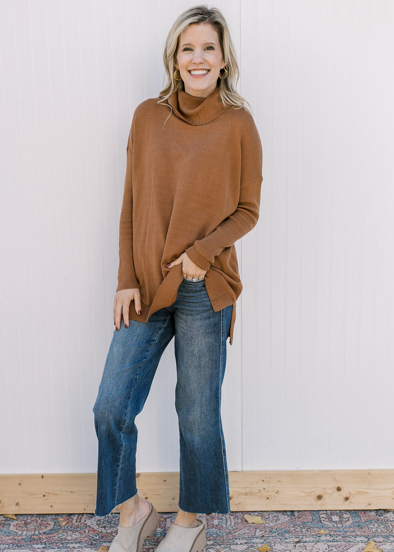 Model wearing a camel flowy sweater with long sleeves, cowl neck and split sides. 