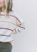 Close up of green, burgundy, gold and red stripes on a cream long sleeve sweater. 