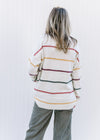 Back view of Model wearing a cream long sleeve sweater with green, burgundy, gold and red stripes.
