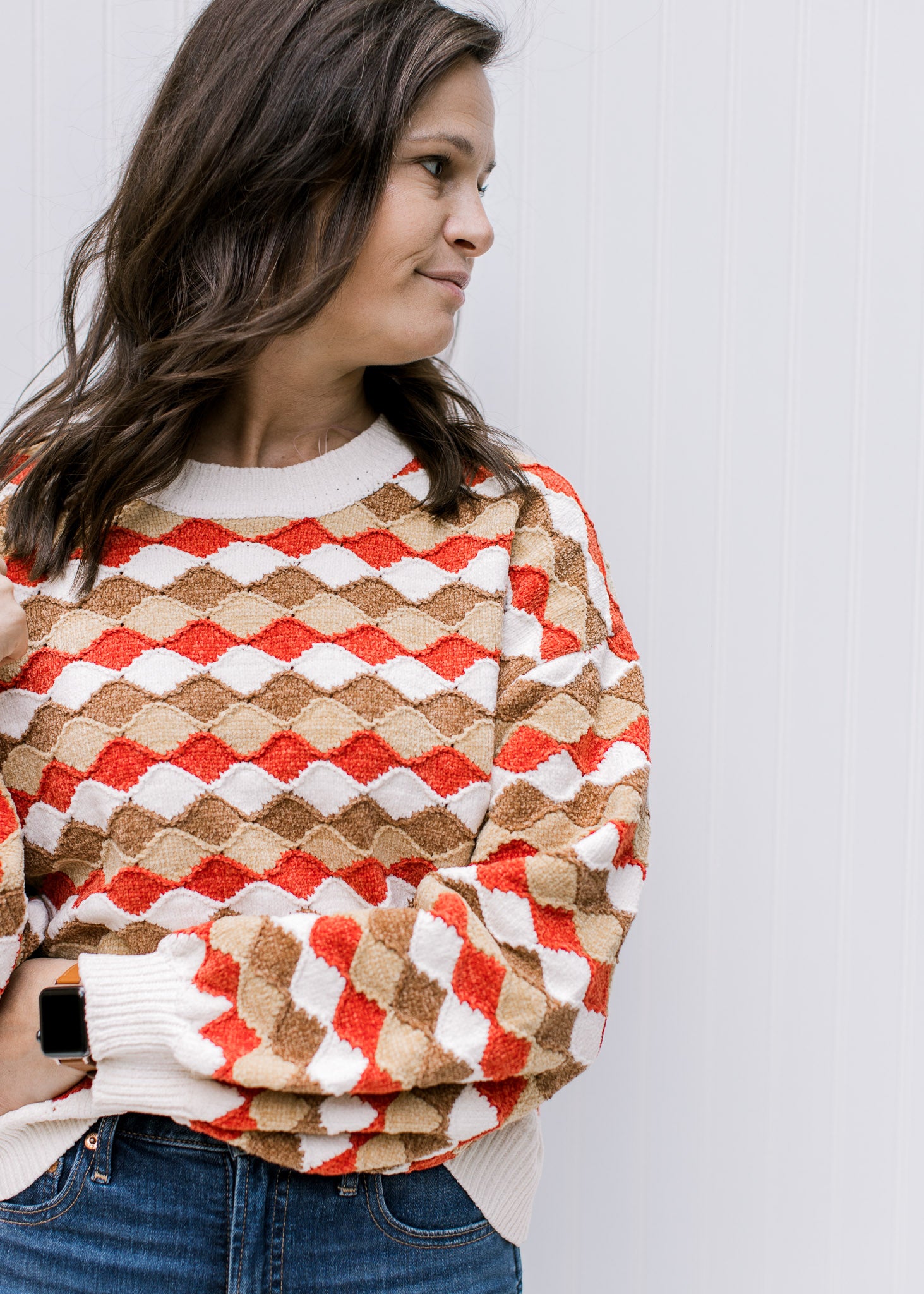 Model wearing a cream, brown, camel and rust wave sweater with bubble long sleeves and a round neck.