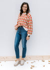 Model wearing jeans with a cream, brown, camel and rust wave sweater with bubble long sleeves. 