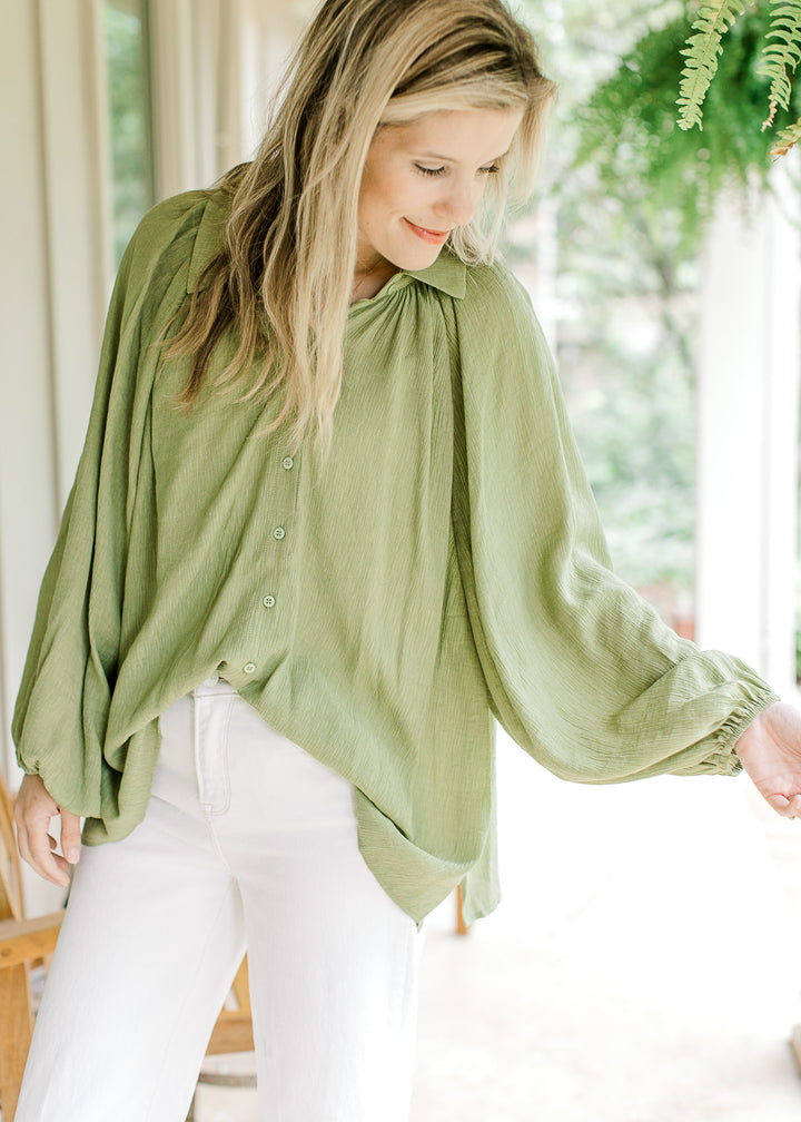 Model wearing an avocado green top with button front, split sides. collar and long sleeve.