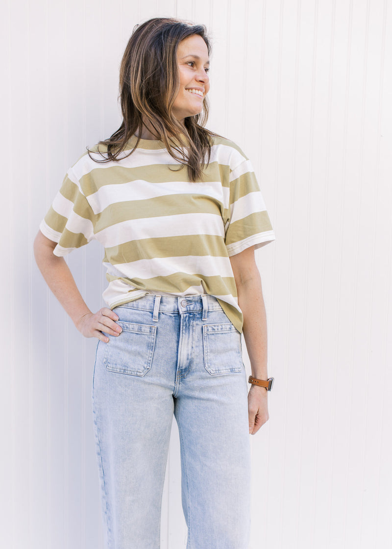 Model wearing jeans with an avocado and cream striped top with a crew neck and short sleeves.