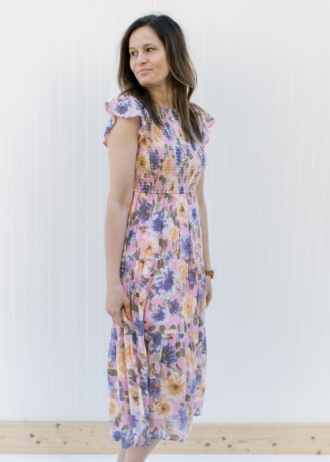 Model wearing a lilac dress with purple, peach and green floral and a smocked bodice.