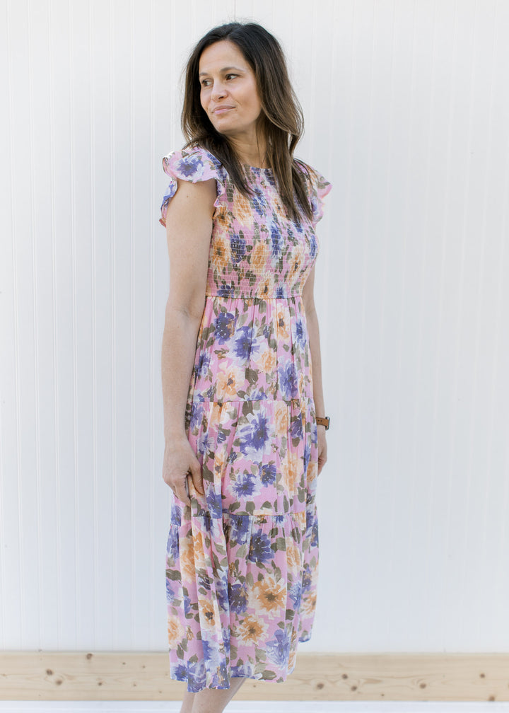 Model wearing a lilac dress with purple, peach and green floral and a smocked bodice.