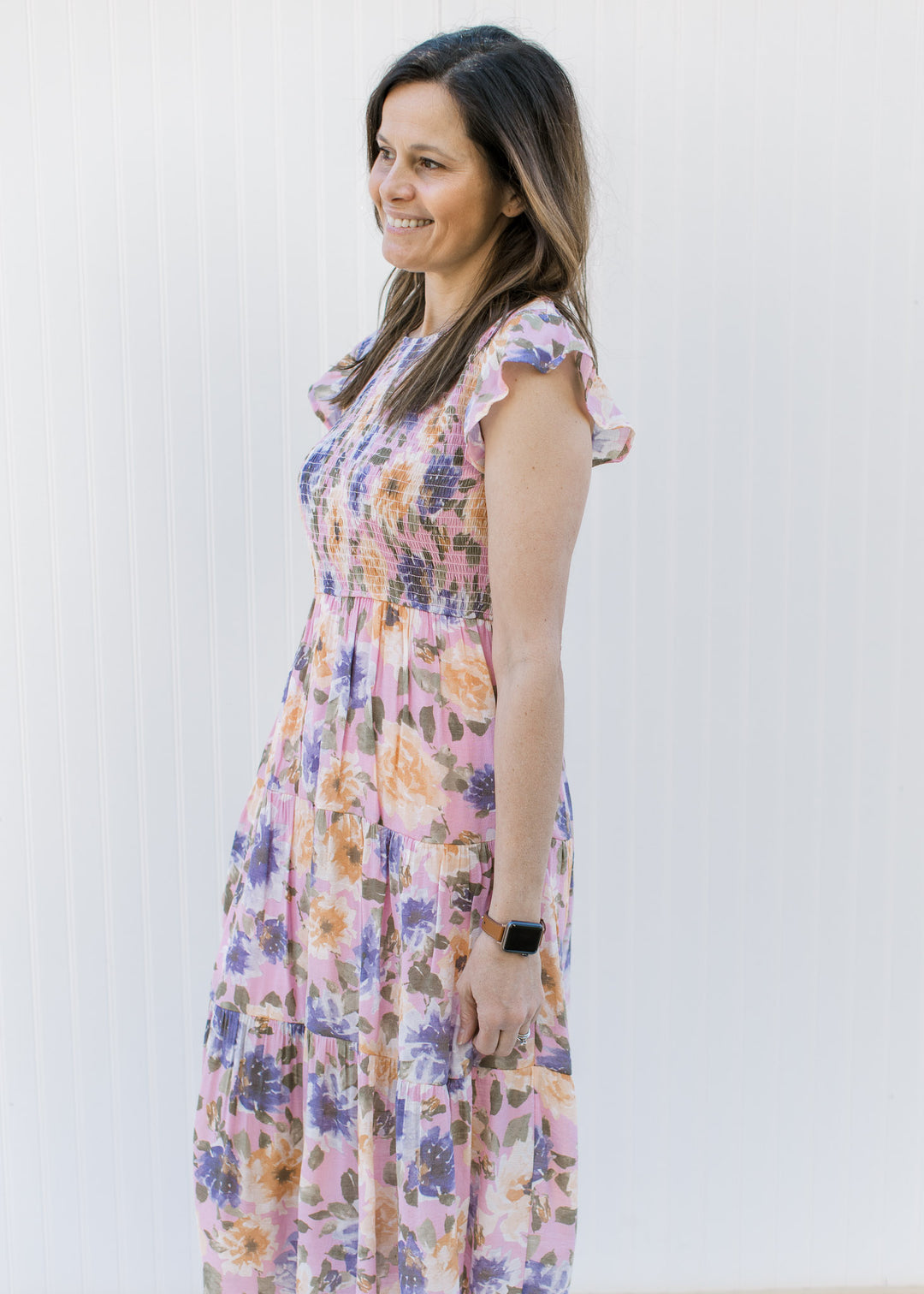 Model wearing a lilac dress with purple, peach and green floral, a smocked bodice and cap sleeves.
