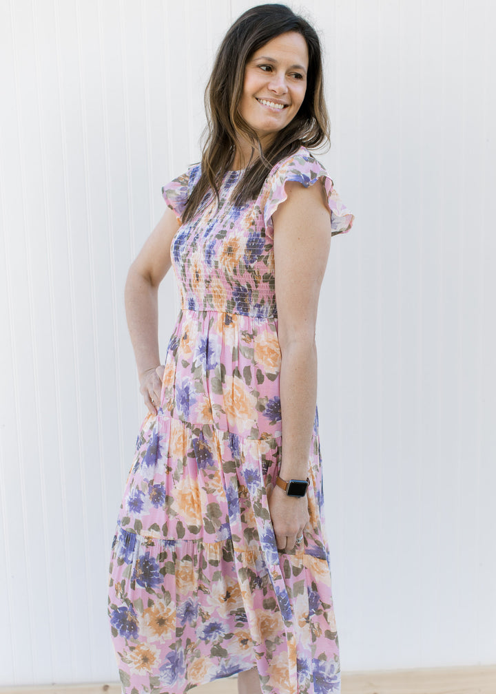 Model wearing a tiered lilac midi with purple, peach and green floral and ruffle cap sleeves.