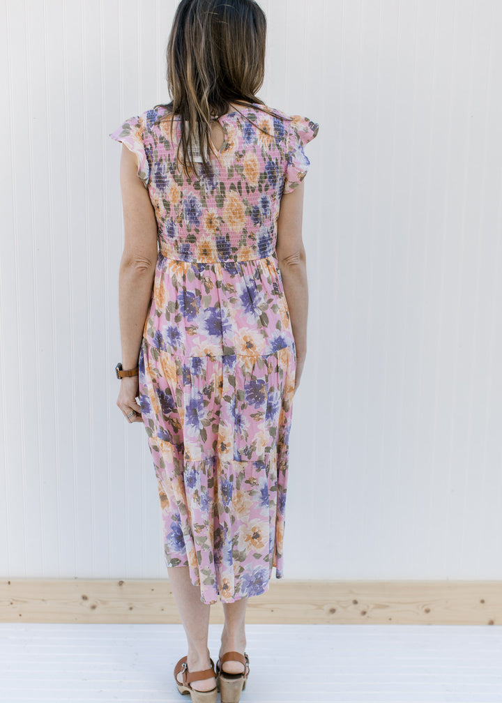 Back view of Model wearing a lilac dress with purple, peach and green floral and a smocked bodice.